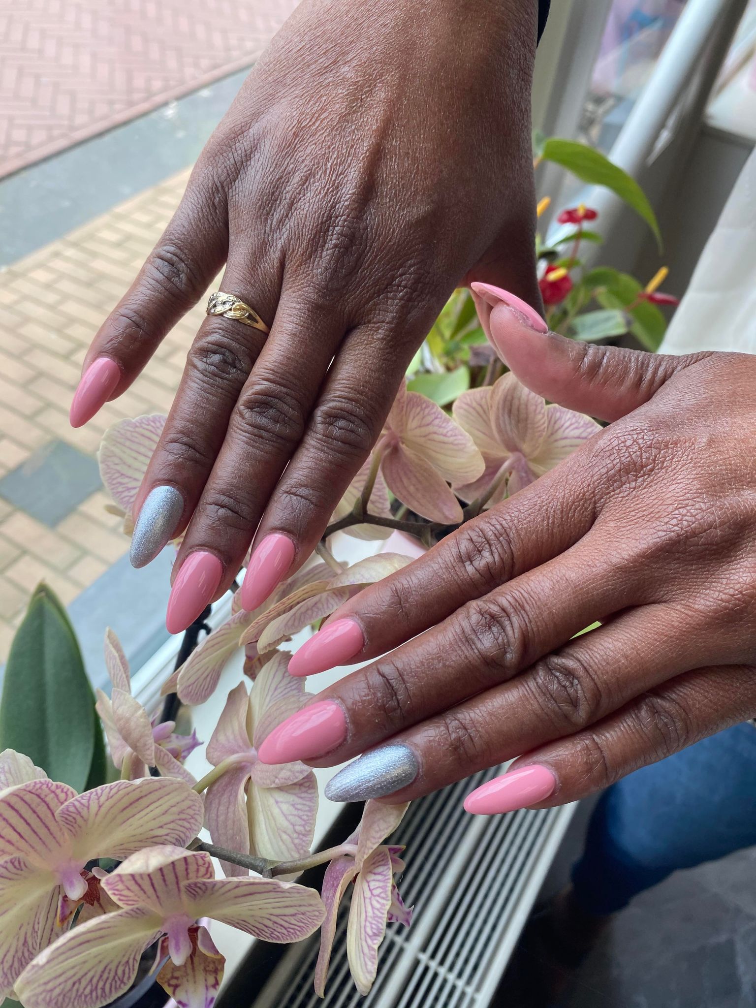 Roze amandelnagels met een zilveren accentnagel, gefotografeerd bij de orchideeën in de etalage van Linh Nails